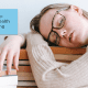 A woman with blonde hair falling asleep on a stack of books, studying about the role of sleep in online learning.